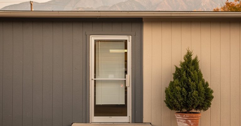 Exterior of a small community clinic building on a quiet Utah morning, Wasatch foothills in the distance under a pale autumn sky